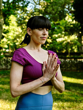 Side view of tranquil woman practicing yoga in Tadasana while standing with closed eyes and Namaste hands in park