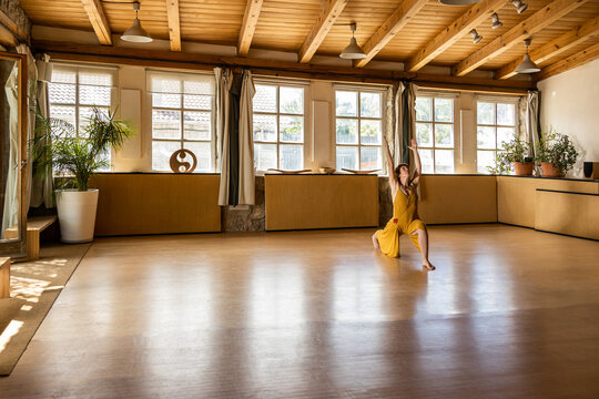 Concentrated female in long waving dressstanding barefoot in studio and practicing yoga in Anjaneyasana