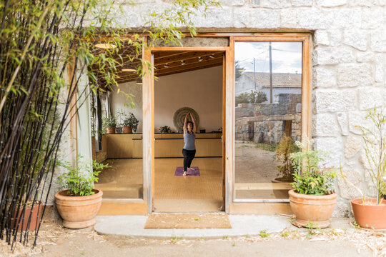 From doorway view of serene female standing in studio doing crescent lunge pose while practicing yoga looking at up