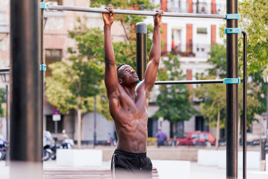 Focused African American male athlete doing pull ups on crossbar during intense training on sports ground in city