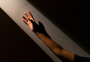 Unrecognizable crop person reaching out hand towards bright light while standing in dark room