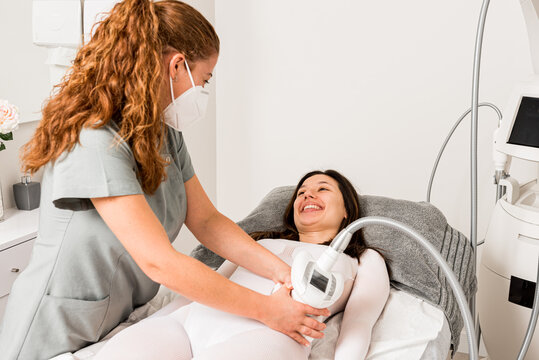 Masseuse in protective mask doing anti cellulite lipo massage to female client waist dressed in white suit during body care procedure in salon of apparatus cosmetology