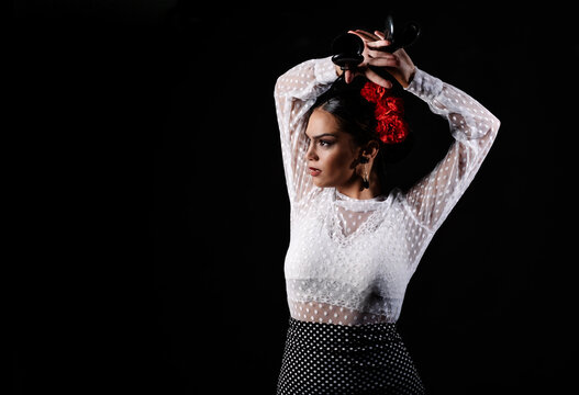 Young Hispanic woman in white blouse performing traditional Flamenco dance with castanets in raised arms