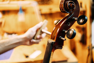 Cropped unrecognizable professional male master using peg hole reamer while repairing and tuning string instrument in workshop