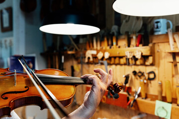 Cropped unrecognizable mature male artisan luthier testing violin after restoration in workshop