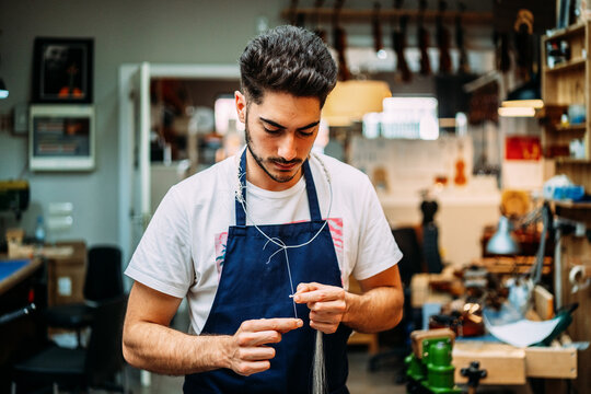 Focused young skilled luthier preparing horsehair for violin bow during restoration work in modern workshop