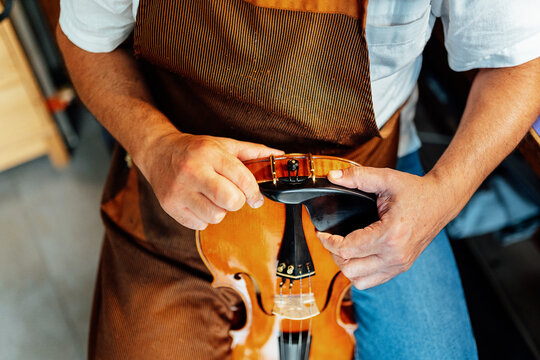 High angle of crop anonymous craftsman holding violin with clamp fixed on lower bout of instrument during restoration work