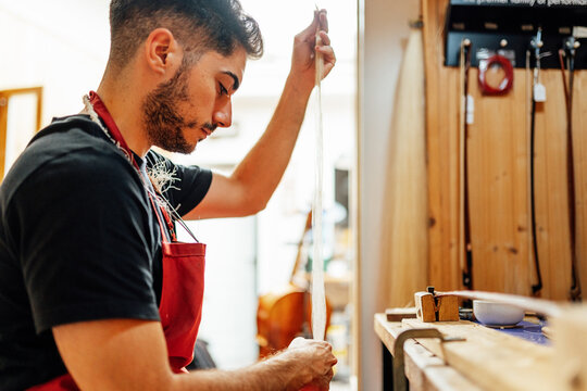 Side view of young male artisan master preparing hank of horsehair for making violin bow in workshop