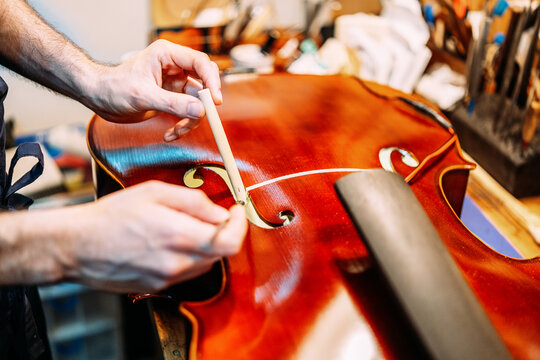Crop anonymous craftsman setting sound post while building string instrument in workshop