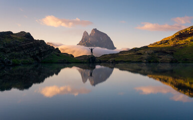 Silhouette of carefree tourist standing with outstretched arms on rock near lake and enjoying freedom in mountains during sunset