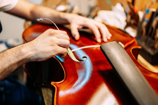 Crop anonymous craftsman setting sound post while building string instrument in workshop