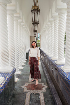 Full body of ethnic female traveler in summer outfit standing in ornamental walkway with stone columns of Omar Ali Saifuddien Mosque during holiday and looking at camera