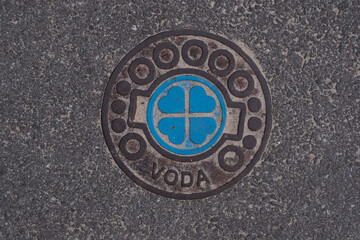 Water line cover on a street with beautiful hearts design and text "VODA" meaning water. Manhole cover-up on a public asphalt city road in Pärnu, Estonia. Attention to detail.
