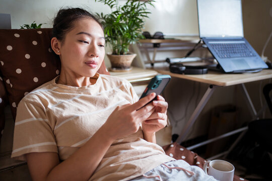 Female sitting on bed in bedroom and choosing food in mobile app via smartphone while shopping online