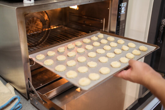 Crop unrecognizable baker in apron placing baking sheet with cookies into preheated oven at home