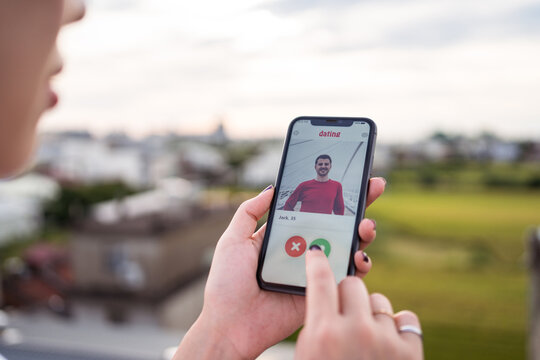 Anonymous woman selecting man while resting on terrace and browsing dating app on smartphone