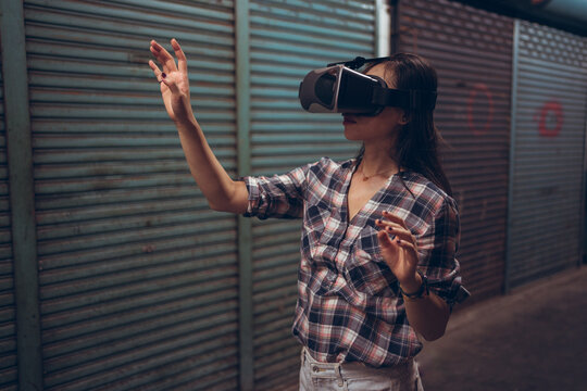 Calm female standing on narrow shabby street and experiencing virtual reality while wearing wireless VR goggles