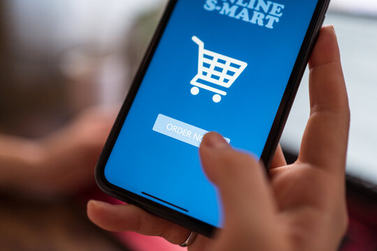 Crop female in domestic wear sitting on bed and ordering food online while using cellphone