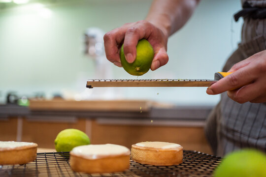 Crop person in apron making tarts with curd and lime zest working at kitchen table