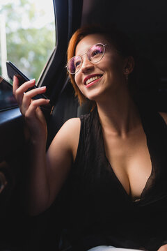 Cheerful female entrepreneur sitting in luxury car and recording voice message while working and using cellphone