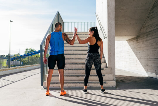 Back view of strong sportsman and sportswoman standing on street and giving high five while looking at each other