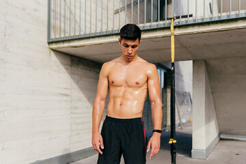 Muscular shirtless male athlete standing resting after hard workout and looking down