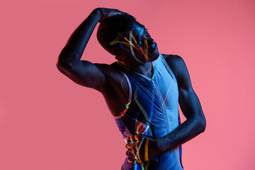 Professional young African American sportsman in active wear performing stretching exercise during training in studio with colorful background and neon lights with eyes closed