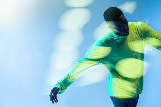 Young muscular African American jogger performing running movements against colorful background in studio with neon illumination