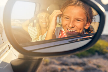 Mirror of a car with the image of a mother and daughter looking at the mirror with the car parked in the middle of nature