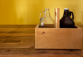 two empty glass half-gallon jugs, one amber, one clear, in a rustic wooden box on top of a wood...