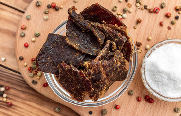 Bowl with beef jerky and spices on wooden background.