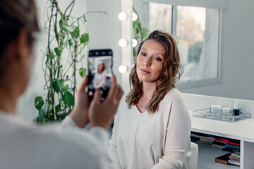 Back view of female makeup artist taking photo of charming woman with professional makeup in beauty salon