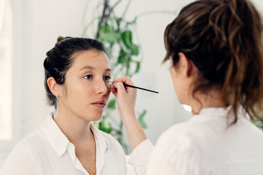 Back view of female makeup artist applying eyeliner on face of professional model in beauty studio
