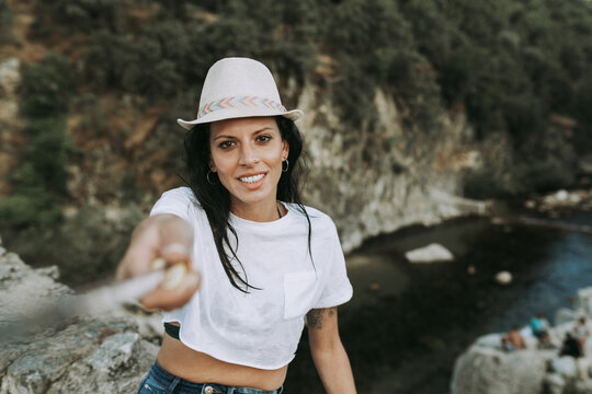Content female tourist using selfie stick and taking photo while standing on hill in mountains and looking at camera during holiday