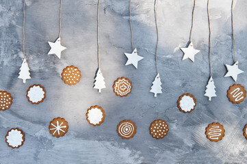Plate with assorted gingerbread cookies with white icing placed near gray wall decorated with craft star and tree shaped paper items