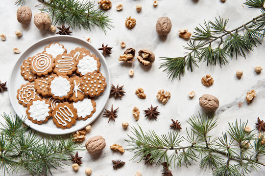 Top view composition with sweet homemade Christmas cookies decorated with white sugar icing served on plate placed on white table near various nuts and fir branch