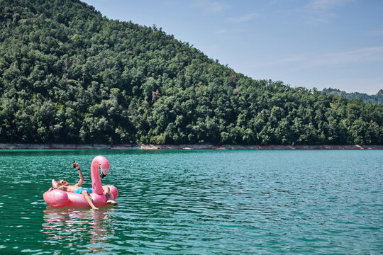 Relaxed male with bottle of refreshing drink lying on inflatable ring in shape of flamingo and floating on lake during summer vacation