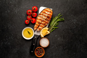 Grilled salmon steak with lemon and rosemary over meat knife on stone background with copy space