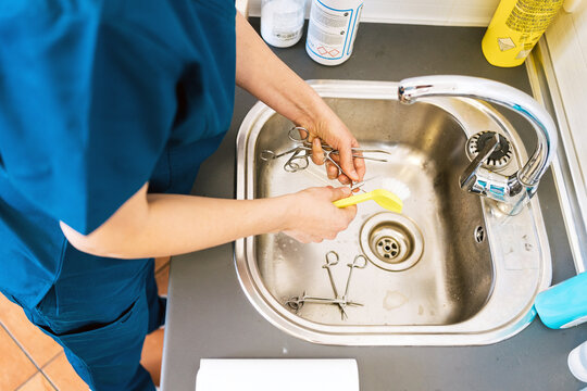 From above anonymous doctor washing surgical tools over sink during work in hospital