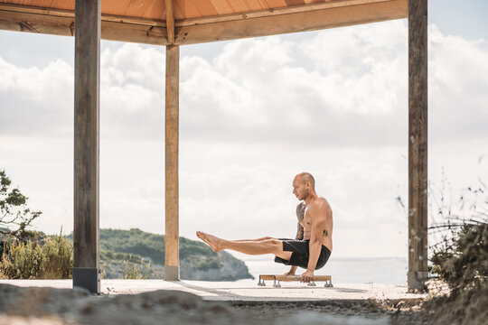 Side view of male athlete with muscular torso performing handstand on parallel bars during workout in summer