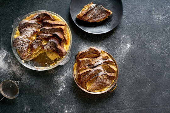 Top view of traditional bread pudding with custard, served with aromatic orange zest butter and powdered sugar on dark background