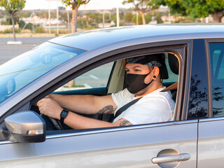 Naklejka premium Hombre joven con mascarilla conduciendo respetando las medidas de seguridad de la pandemia del coronavirus