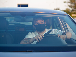 Hombre joven con mascarilla conduciendo respetando las medidas de seguridad de la pandemia del...