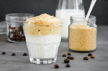 Iced Dalgona Coffee, a trendy fluffy creamy whipped coffee with milk in a glass on a dark background. Horizontal, copy space.