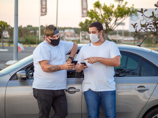 Fototapeta premium Dos hombres jóvenes utilizando el teléfono móvil apoyados en un coche 