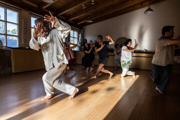 Full body of mature male instructor with group of diverse people performing chi kung pose during practice in studio