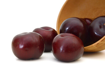 Red plum fruit isolated in wooden bowl on white background