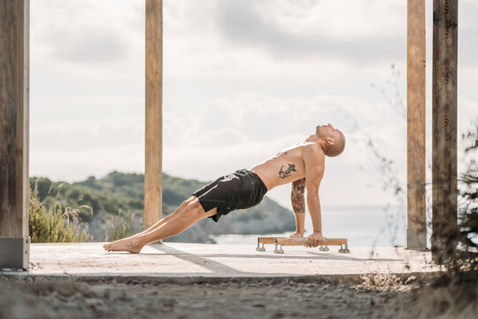 Side view of male athlete with muscular torso performing handstand on parallel bars during workout in summer