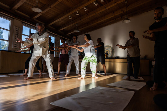 Group of people with instructor performing flowing movements with outstretched arms during chi kung practice in studio