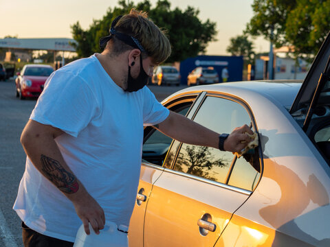 Hombre joven con tatuajes limpiando las ventanillas del coche